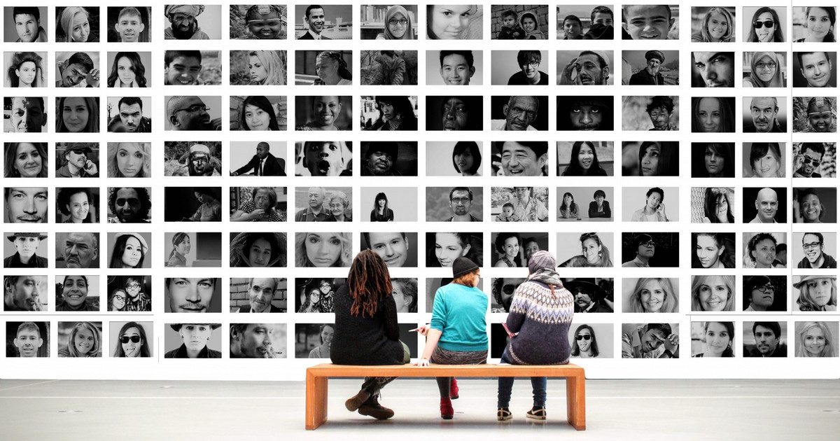 Drei Personen sitzen vor einer großen Collage, die eine Vielzahl von Porträts zeigt