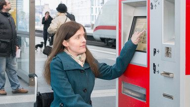 Frau im Rollstuhl am Fahrkartenautomat