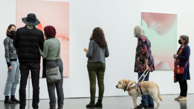 Mehrere Personen (u.a. mit Blindenhund) betrachten ein Bild.